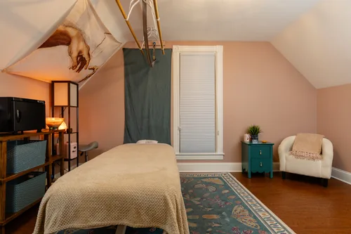 Treatment room with warm lamplight, seating for a guest, and a private window